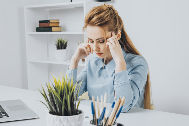 Young office girl sitting at her workplace feeling bad. Woman has a headache. - Foto, Imagen