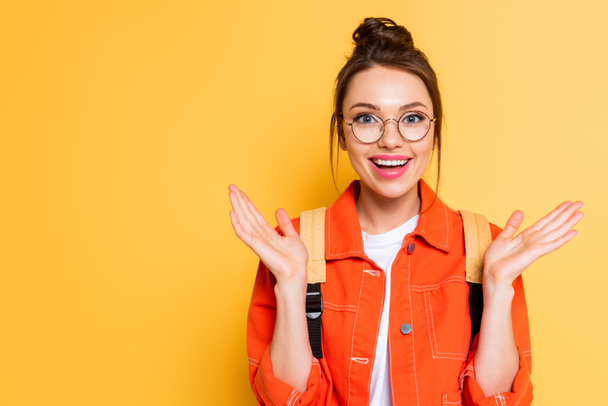 happy student in eyeglasses smiling while standing with open arms isolated on yellow - Zdjęcie, obraz
