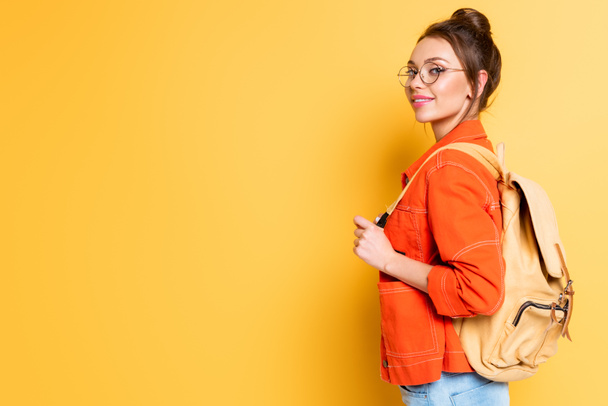 atraente, estudante sorridente com mochila olhando para a câmera no fundo amarelo
 - Foto, Imagem
