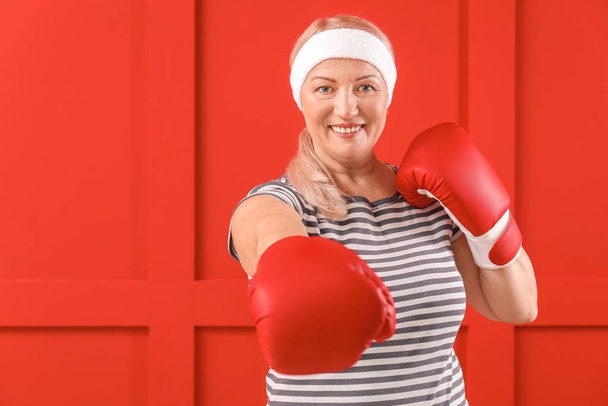 Αθλητική ώριμη γυναίκα σε γάντια πυγμαχίας στο φόντο χρώμα - Φωτογραφία, εικόνα