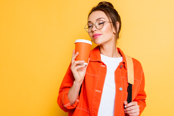 étudiant joyeux dans les lunettes profitant saveur de café avec les yeux fermés isolé sur jaune
 - Photo, image