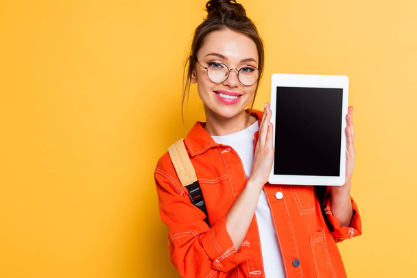 cheerful student in eyeglasses showing digital tablet with blank screen on yellow background - Photo, Image