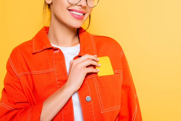 обрезанный вид улыбающегося студента, достающего смартфон из кармана, изолированного на желтом
 - Фото, изображение