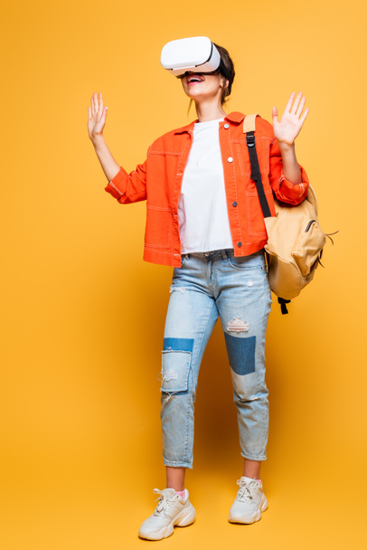 excited student with backpack gesturing while using vr headset on yellow background - Foto, Imagem