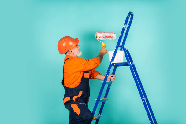 Bearded worker. senior man painter use roller on ladder. painting the wall in blue. professional painter in working clothes. worker painting wall in room. male decorator painting with roller - Foto, Bild