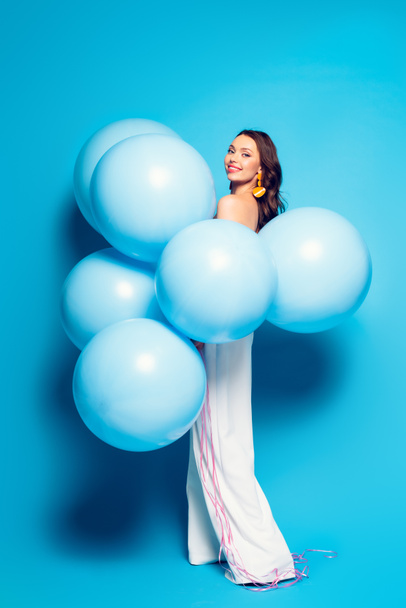 volledige weergave van gelukkig elegante vrouw met grote feestelijke ballonnen glimlachen op camera op blauwe achtergrond - Foto, afbeelding
