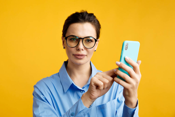 Επιχειρηματίας σε γυαλιά χρησιμοποιώντας τηλέφωνο απομονωμένο πάνω από το κίτρινο φόντο. - Φωτογραφία, εικόνα