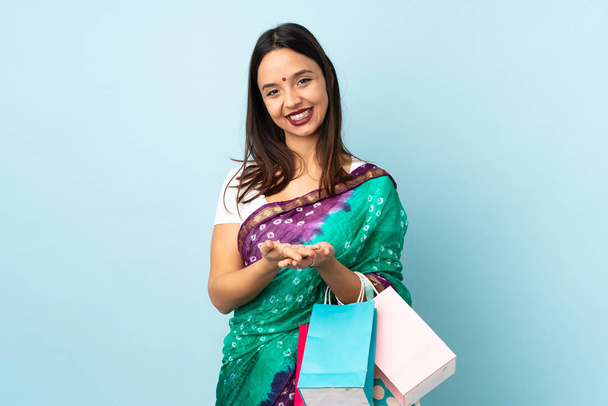 Jovem indiana com sacos de compras segurando copyspace imaginário na palma da mão para inserir um anúncio
 - Foto, Imagem