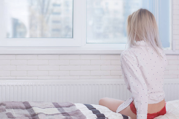 Девушка сидит на кровати и смотрит в окно
 - Фото, изображение