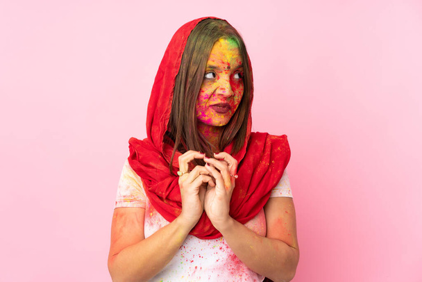 Mujer india joven con coloridos polvos de holi en su cara aislada sobre fondo rosa maquinando algo
 - Foto, imagen
