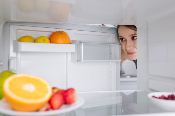 selective focus of girl looking at fruits in fridge  - Foto, afbeelding