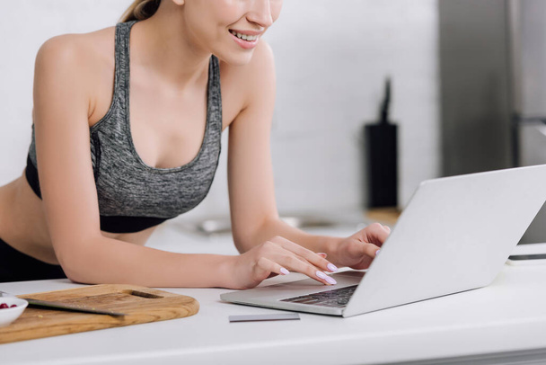 przycięty widok wesołej dziewczyny wpisując na klawiaturze laptopa w pobliżu karty kredytowej  - Zdjęcie, obraz
