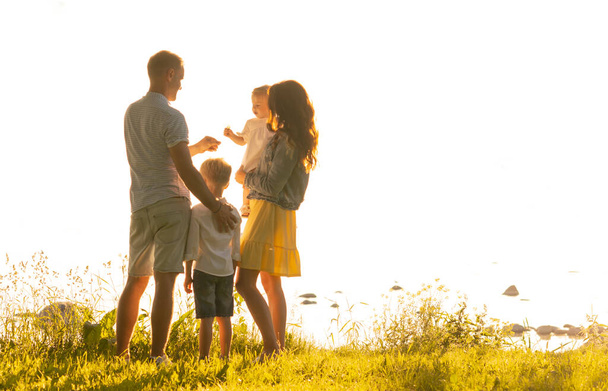 Glücklich liebende Familie, die im Licht des Sonnenuntergangs im Freien spazieren geht. Vater, Mutter, Sohn und Tochter. Hintergrund Meer und Feld - Foto, Bild