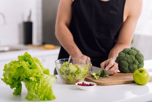 cropped view of man cutting broccoli on chopping board  - Foto, afbeelding