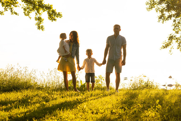 Joyeux famille aimante marchant en plein air à la lumière du coucher du soleil. Père, mère, fils et fille. Mer et terrain fond
 - Photo, image
