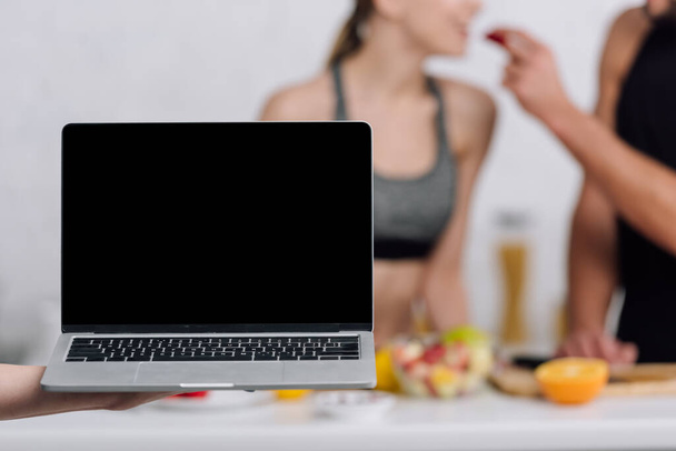 selective focus of laptop with blank screen near couple in kitchen  - Foto, Bild