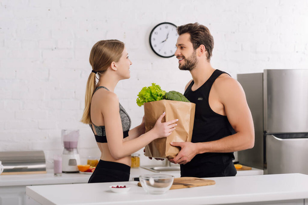 boční pohled na šťastnou dívku a vousatý muž držící papírový sáček s potravinami  - Fotografie, Obrázek