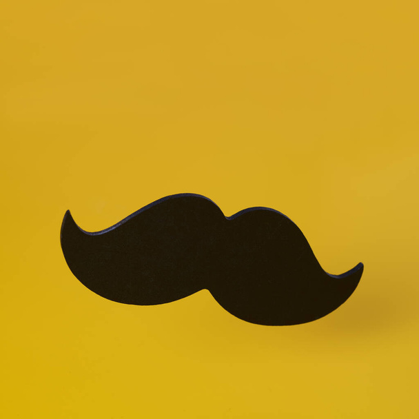 Nahaufnahme eines schwarzen Schnurrbarts auf gelbem Hintergrund mit etwas Leerstelle an der Spitze - Foto, Bild