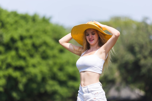 retrato hermosa joven rubia pelo sonrisa con sombrero amarillo posando al aire libre en jardín verde
. - Foto, Imagen