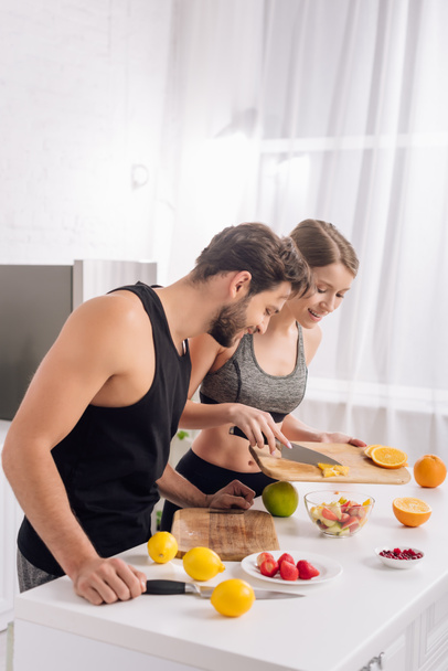 gelukkig man op zoek naar vrouw koken fruit salade  - Foto, afbeelding