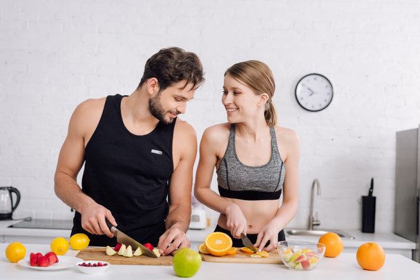 cheerful couple smiling while preparing fruit salad  - Photo, Image