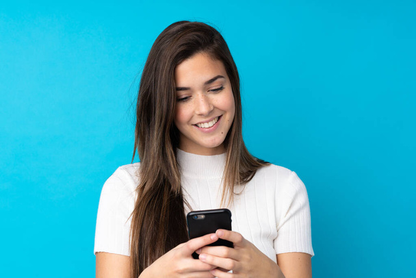 Teenager dívka přes izolované modré pozadí odesílání zprávy s mobilním - Fotografie, Obrázek