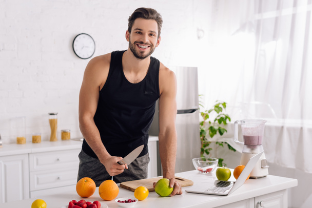 happy man cooking near laptop and blender in kitchen  - Photo, Image