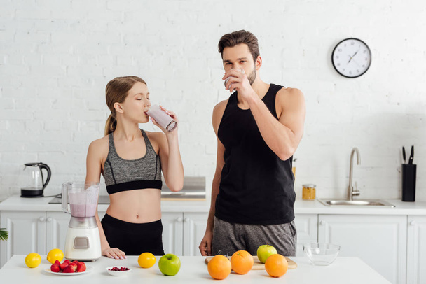 sportive man and woman drinking tasty smoothie near fruits  - Фото, изображение