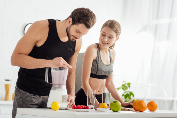 спортивный человек готовит смузи рядом счастливая девушка и фрукты
  - Фото, изображение