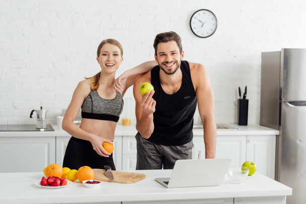 happy man and woman with tasty fruits looking at camera near laptop  - 写真・画像