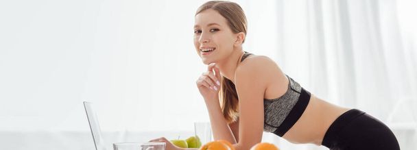 panoramic shot of happy girl near laptop and fruits  - Фото, изображение