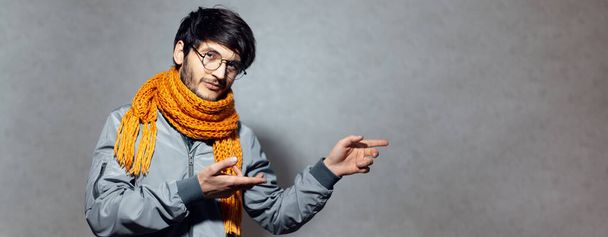 Портрет молодого парня, одетого в шарф, очки, показывающего руки на пустом пространстве
. - Фото, изображение