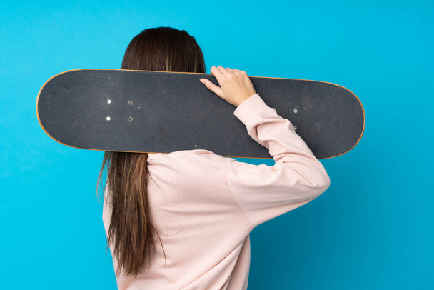 Teenager girl over isolated blue background with a skate in back position - Foto, Imagem