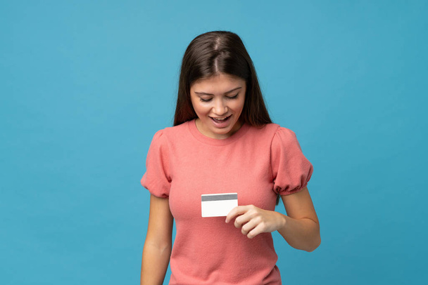 Молодая женщина на изолированном синем фоне держит кредитную карту
 - Фото, изображение