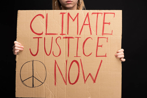 Partial view of blonde woman holding placard with climate justice now lettering isolated on black, global warming concept - Photo, Image