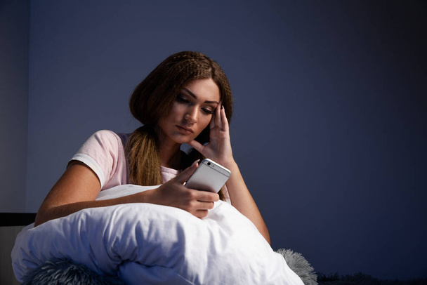 Yatakta yastıkla oturup telefonla konuşan yorgun bir kadın.. - Fotoğraf, Görsel