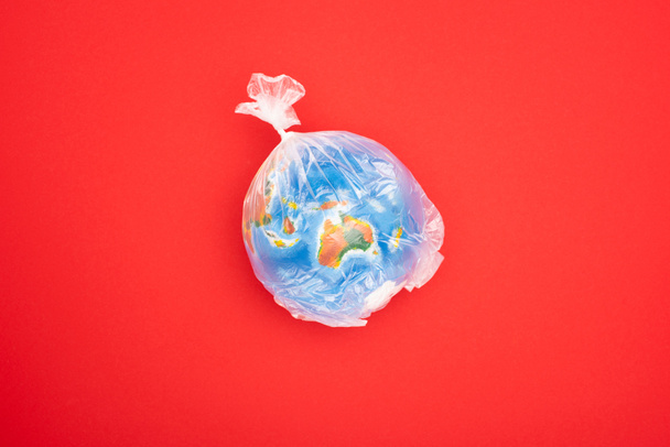 Weltkugel von oben in Plastiktüte isoliert auf rotem, globalem Erwärmungskonzept - Foto, Bild