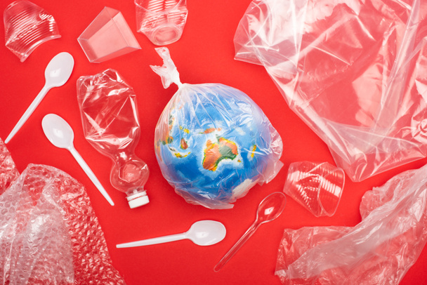 Top view of globe in plastic bag with garbage around isolated on red, global warming concept - Photo, Image