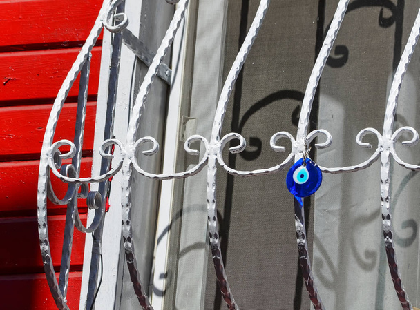 Colgante de cristal redondo azul en forma de ojo colgando de una ventana de celosía. Amuleto turco tradicional - Nazar boncuk
. - Foto, imagen