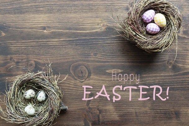 bird nests with colorful painted eggs and text happy easter on wooden background, holiday concept  - Fotografie, Obrázek