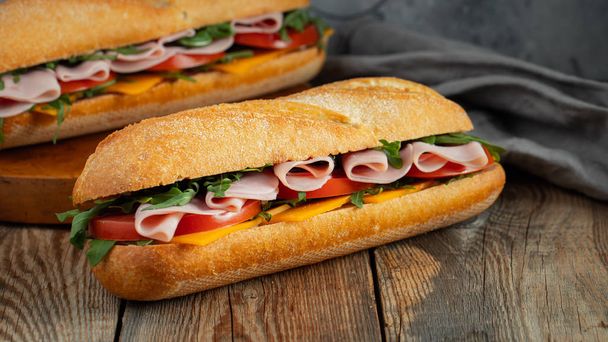 Two Long baguette Sandwiches with arugula, slices of fresh tomatoes, ham and cheese. - Photo, Image