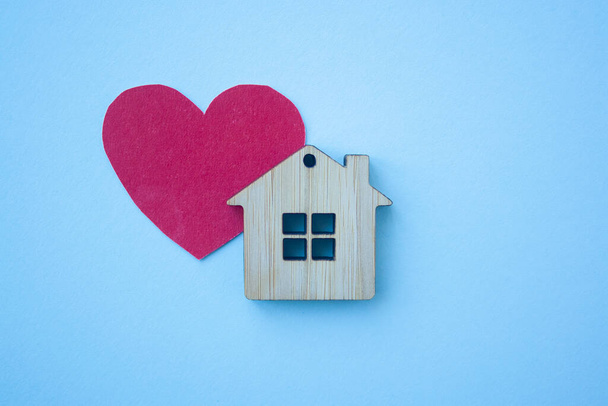 Love home, insurance and mortgage, marriage and valentine concept. Small wooden house toy and paper heart shape on blue background top view  - 写真・画像
