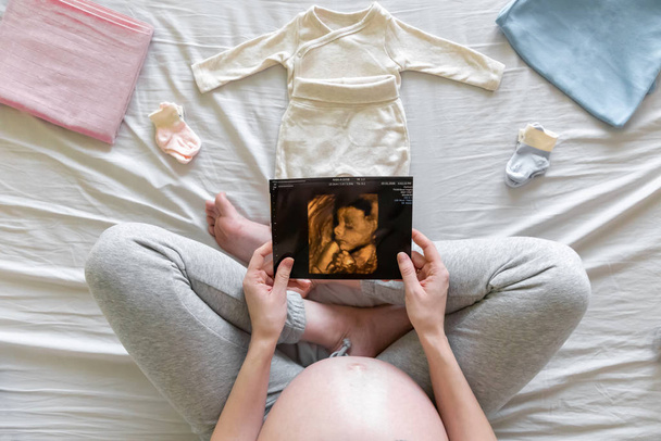 Vista superior de la mujer embarazada embarazada en la cama mirando ecografías en el hogar, niño o niña, embarazo y concepto de nacimiento
 - Foto, Imagen