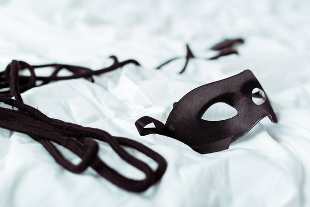 selective focus of eye mask and black rope on white bedding  - Foto, immagini