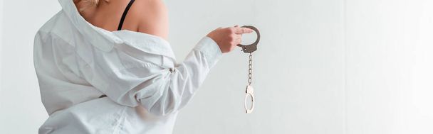 panoramic shot of young woman in shirt holding handcuffs  - Photo, Image