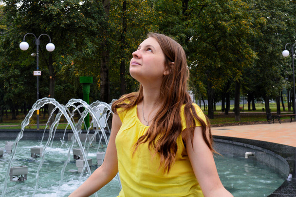 Woman with dark hair in a yellow T-shirt near the fountain - Foto, imagen