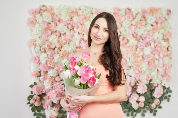 Beautiful girl with tulip flowers in hands on floral background. Greeting card for Women's Day March 8 or Mother's Day.Very nice florist woman holding beautiful colourful blossoming flowers bouquet. - 写真・画像