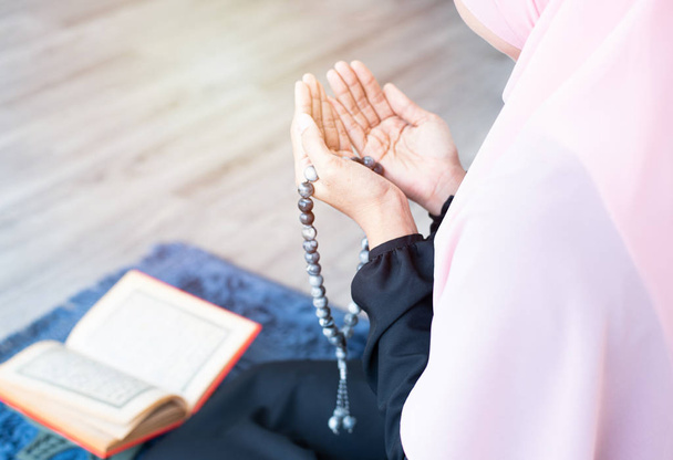 side of asian young beautiful muslim woman pray with beads and read quran sit on carpet mat with meditation in mosque. - Photo, image