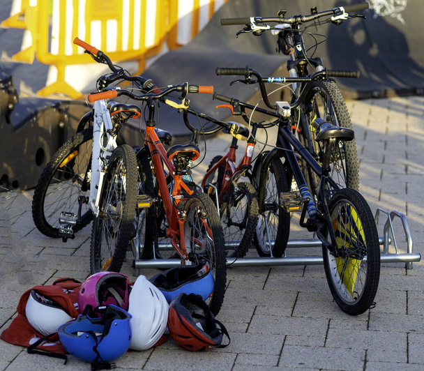 Детские велосипеды, припаркованные на эстакаде, и разноцветные шлемы, лежащие на земле - Фото, изображение