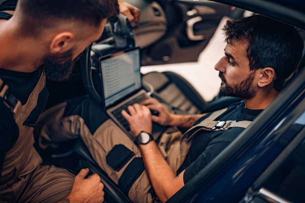 At the car service.Two auto mechanics doing diagnostics with laptop.Car service, repair and people concept. - Photo, Image